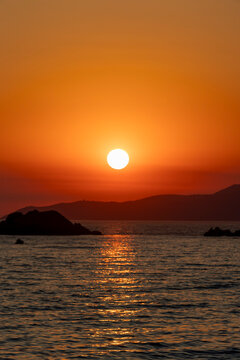 A serene sunset over the rocky seashore with vibrant orange and red hues, Budva, Montenegro