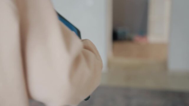 Caucasian woman picks up tablet and folder from desk, turns away from workspace, walks through doorway past cabinet, intimate detailed focus on hands and materials, subtle finishing mood
