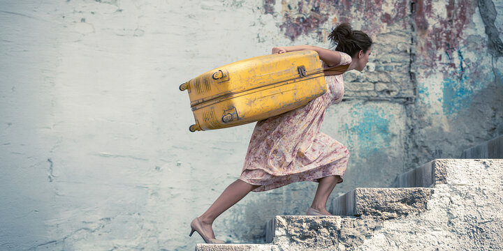 A woman struggling to carry a heavy yellow suitcase up a weathered stone staircase, her determined expression suggesting a difficult journey