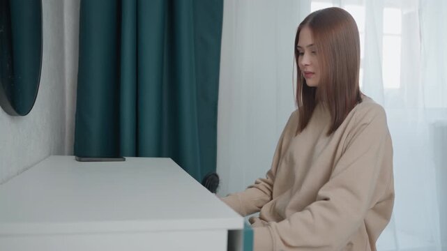 Young woman sits at desk, home tutor rehearsing grammar exercises, checking notes and tablet, calm daylight, teal curtain, minimal modern interior, focused preparation for online lesson
