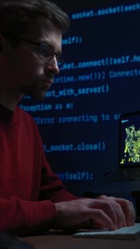 Concentrated male coder in glasses works at a dark office desk, surrounded by screens filled with programming code and graph, absorbed in solving a complex AI or data science problem late at night.