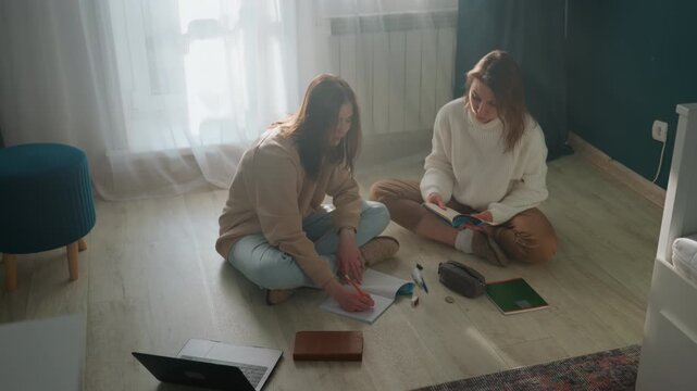 Women preparing for exam together on floor with notebooks and laptop, active peer coaching and grammar practice, highlighters and pens spread out, collaborative notetaking, energetic yet calm study