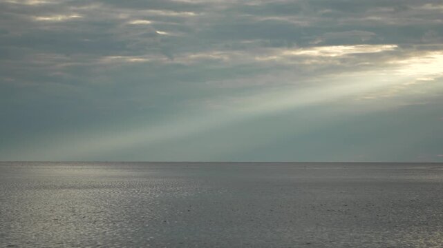 Sunbeams clouds ocean dramatic crepuscular rays shining onto the tranquil gray sea surface.