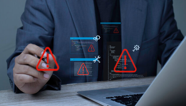 Programmer holding pen pointing at warning alert icon to fix bugs in software source code. Concept of debugging, system error warning, software development, and technical troubleshooting on laptop.
