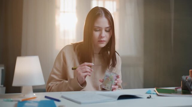 White woman taking reward from jar, language coach marking progress, dipping spoon into candy jar, smiling over completed worksheet, warm window light, desk lamp illuminating papers and pens, potted