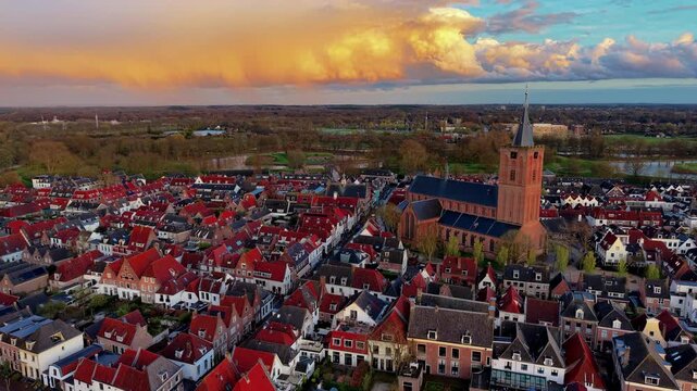 Aerial view video clip of historic Naarden fortified town center, red tiled roofs, Grote Kerk church tower, dramatic golden sunset clouds, and moat countryside in North Holland, Netherlands