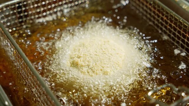 Breaded food balls being fried in hot oil in a deep fryer. Deep frying concept.