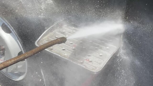 commercial truck metal step platform pressure wash during carwash process showing undercarriage chassis of heavy duty vehicle for cleaning maintenance inspection outdoor station.