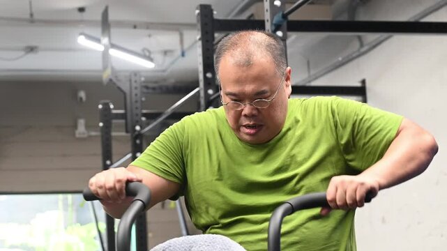 Exercise for overweight man pedaling stationary bike in gym for indoor cycling cardio workout focused on effort determination and endurance improving fitness and showing sweat