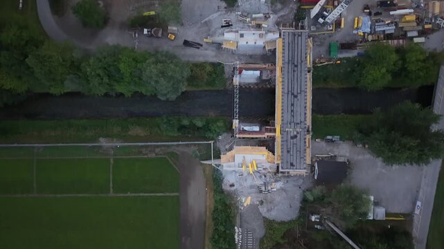 Top-down aerial view of a railway construction site where a new bridge is being built over a small river, with the existing rail line temporarily interrupted by construction.