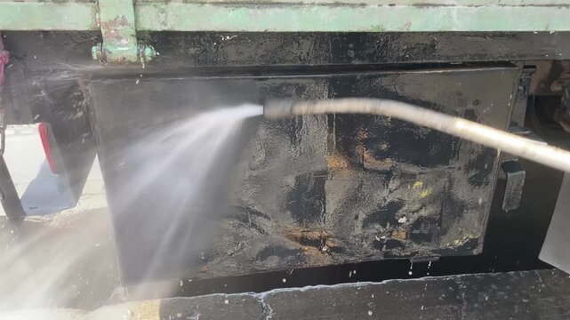 commercial truck heavy water spray mist underbody during carwash process showing undercarriage chassis of heavy duty vehicle for cleaning maintenance inspection outdoor station.