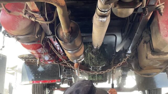 commercial truck exhaust pipes vertical water during carwash process showing undercarriage chassis of heavy duty vehicle for cleaning maintenance inspection outdoor station.