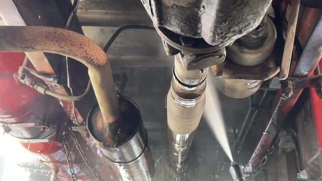 commercial truck exhaust pipes water spray mist during carwash process showing undercarriage chassis of heavy duty vehicle for cleaning maintenance inspection outdoor station.