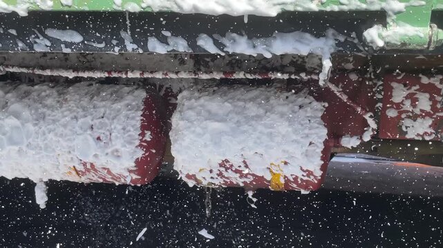commercial truck red tank under heavy water foam during carwash process showing undercarriage chassis of heavy duty vehicle for cleaning maintenance inspection outdoor station.