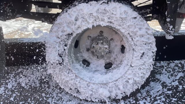 commercial truck wheel hub heavy water pressure during carwash process showing undercarriage chassis of heavy duty vehicle for cleaning maintenance inspection outdoor station.