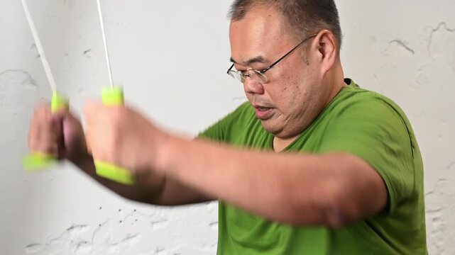 Exercise for overweight man in indoor studio wearing green t shirt doing seated stretch and indoor workout with focused expression showing effort and motion against textured wall for fitness
