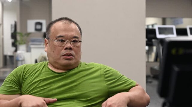Overweight man indoor gym workout on treadmill and cardio machines wearing green shirt focused expression. seated exercise, breathing hard for fitness, healthy cardio endurance training