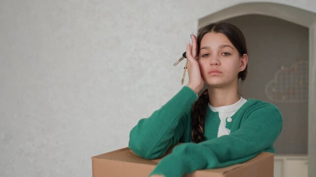 Young woman holding keys over cardboard box, distant expression and thoughtful posture quiet apartment interior, empty walls, moving boxes around, hesitant acceptance, small domestic details
