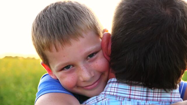 Young dad holding in hands his happy small son at countryside. Little smiling boy looking into camera and hugging his father against bright sunlight at background. Concept of family resting. Close up