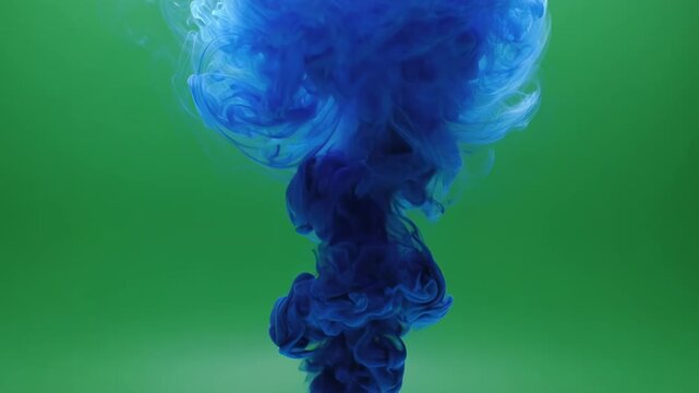 Blue ink cloud blooming in water during studio filming with green screen backdrop