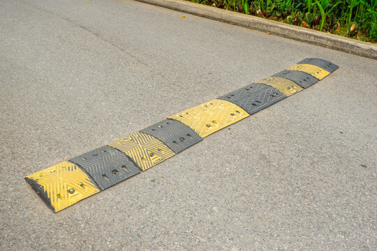 Stripped yellow and black speed bump in the road,Road Speed Bump with Reflective in a sunny day,residential street or parking lot, traffic calming measure to reduce vehicle speeds concept.