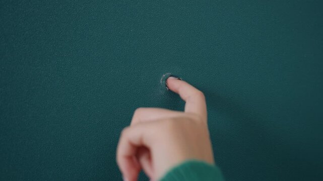 Finger poking hole in teal wall while unpacking during movein green sleeve visible as curious fingertip probes tiny opening interior apartment scene feels playful and investigative, closeup detail