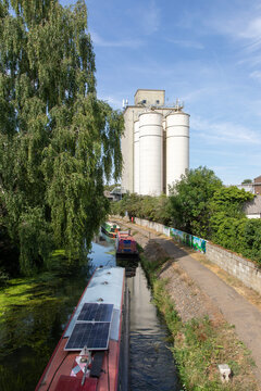 Narrow boats on the River Stort, a canalised river with a towpath, near grain silos in Bishops Stortford, Hertfordshire, England