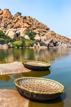 Traditional round wicker coracle boats moored on the shore of the Tungabhadra River amidst ancient granite boulders in Hampi, India. Scenic landscape view, historic travel destination and tourism.