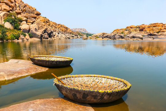 Traditional round wicker coracle boats moored on the shore of the Tungabhadra River amidst ancient granite boulders in Hampi, India. Scenic landscape view, historic travel destination and tourism.