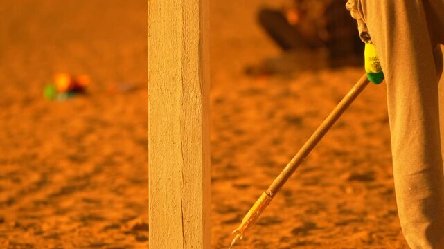 Manual labor painting a wooden pillar with white primer on a sunlit beach. Close-up static shot.