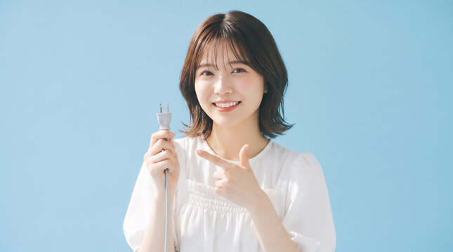 Smiling young Japanese woman pointing at power plug held in hand on blue background