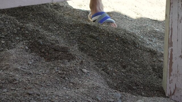 Shoveling gravel debris, a worker uses a metal spade to clear sand under a wooden frame. Static eye-level shot.
