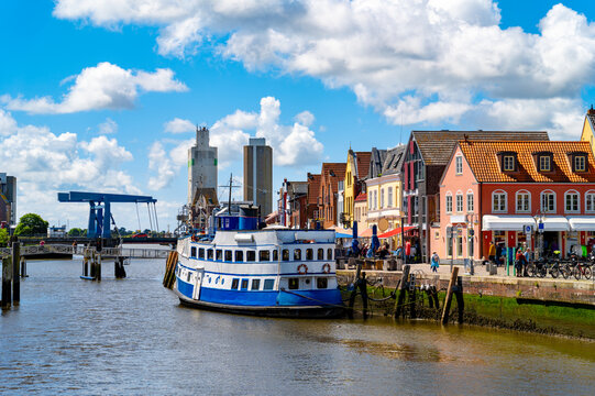 Moored restaurant ship in Husum's historic inner harbor with colorful gabled houses along the waterfront on a sunny summer day.