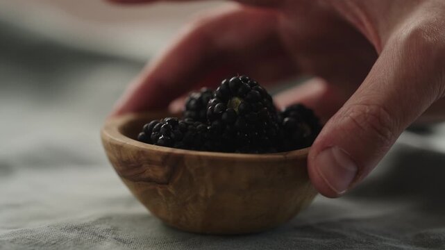 Slow motion man hand put fresh ripe blackberry in a small wooden bowl