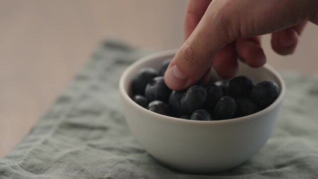 Slow motion man hand take blueberries from a ceramic bowl