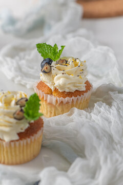 Cupcakes with white frosting and blueberries on white fabric background