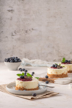 Mini cheesecakes with fresh blueberries and berry compote on a light rustic table