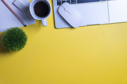 Top view of a bright yellow office desk workspace with a laptop, coffee cup, notebook, and a small green plant. Concept of work from home, creative freelance, and productivity with copy space.