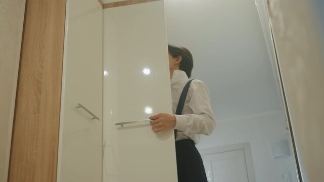 Man adjusting suspenders at closet doorway firm grip on jacket, smooth fabric, focused gaze, quick precise movements, readying for presentation, overhead lights, reflective surfaces, modern corridor,