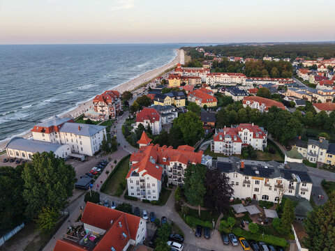 Drone view  Ostseebad Kuhlungsborn resort, Baltic beach, promenade, Ferris wheel, hotels, and red roofs at dusk. Calm coastline, beach chairs, seaside tourism, and summer mood shape scenic cityscape