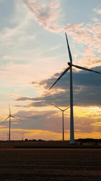 Sunset turbines in the countryside. Wind turbines stand tall as the sun sets behind the clouds in the countryside. The sky shows orange and blue colors.
