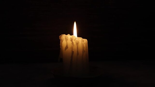 Lit white candle, dark background, close-up.