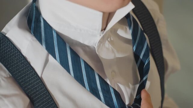 Closeup of anxious man preparing for interview. Man in white shirt fixing striped tie with focused expression. Young man meticulously smoothing his tie and suspenders in soft morning light
