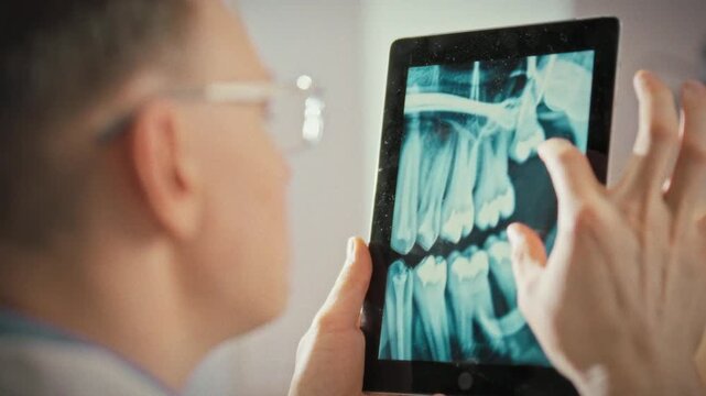 In modern dental clinic, dentist reviews high-resolution tablet with panoramic image of teeth, assessing tooth positions, root details, overall jaw condition, showcasing advanced dental technology