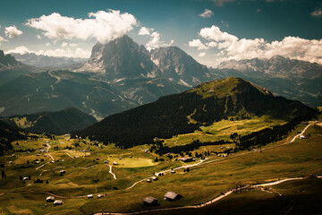 Obraz premium Panoramic view of Sassolungo and Sasso Piatto mountain massif from Seceda in Dolomites, Italy, with green alpine meadows, forested slopes, mountain huts and hiking trails