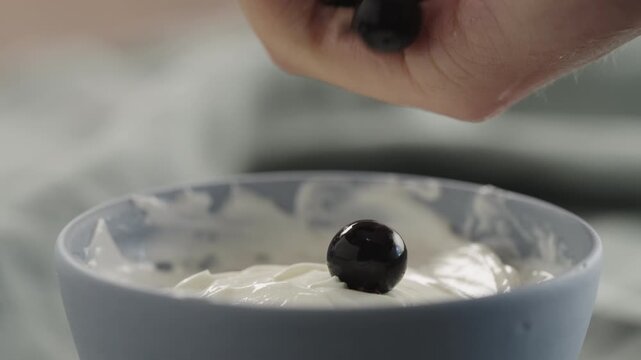 Slow motion man hand add ripe blackcurrant to yogurt in a bowl