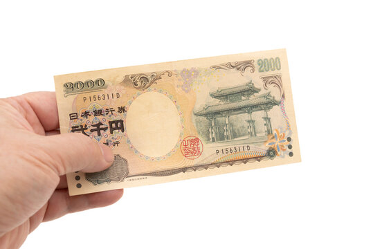 A hand holding a rare 2,000 Japanese yen banknote (front side displaying Shureimon gate). Scarce currency in circulation. Isolated on white background. Symbolizes finance, wealth, and collectibles.