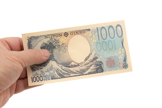 A hand holding the reverse side of a new 1,000 Japanese yen banknote displaying The Great Wave off Kanagawa and Mount Fuji. Latest Series E currency. Isolated on white background.