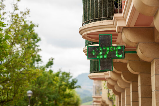 Close-up of a digital street thermometer on a city building showing 27 degrees Celsius