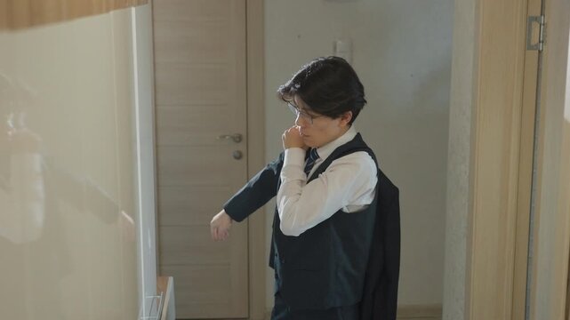 Young man donning jacket at door, straightening tie and vest while glancing at reflection and phone brisk decisive movements suggest final preparations for presentation or meeting, tailored suit
